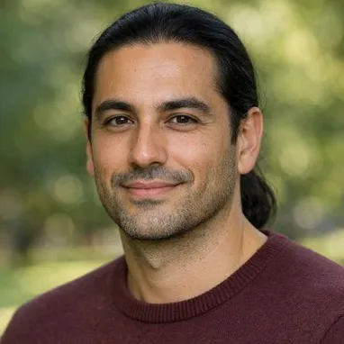 Man in his late 30s, olive skin, black hair in low ponytail, calm expression